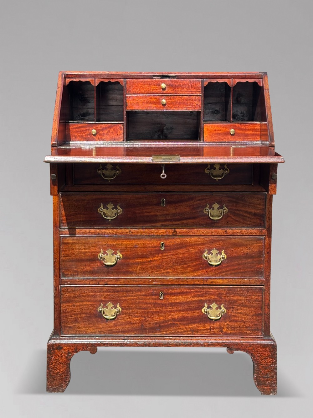 An 18th-century George III mahogany bureau featuring an open sloping slant front revealing small drawers and pigeonholes above four long drawers on bracket feet.
