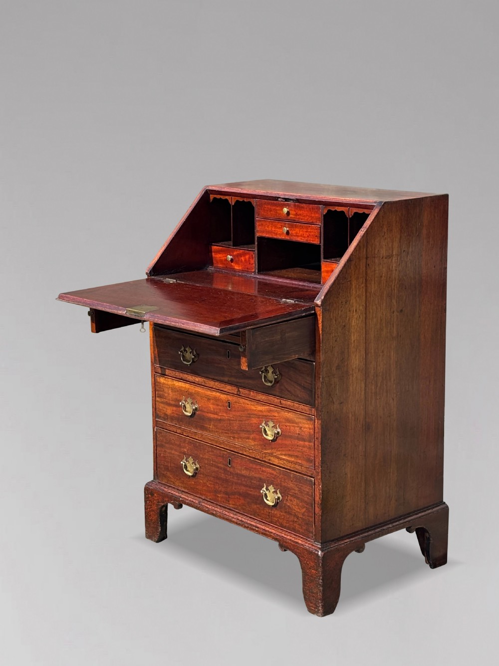 An 18th-century George III mahogany bureau featuring an open sloping slant front revealing small drawers and pigeonholes above four long drawers on bracket feet. View IV