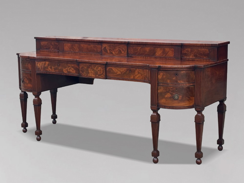 An 18th-century George III flame mahogany sideboard featuring a raised stage back, oval wood inlays, fluted side columns, and six turned reeded legs. View III