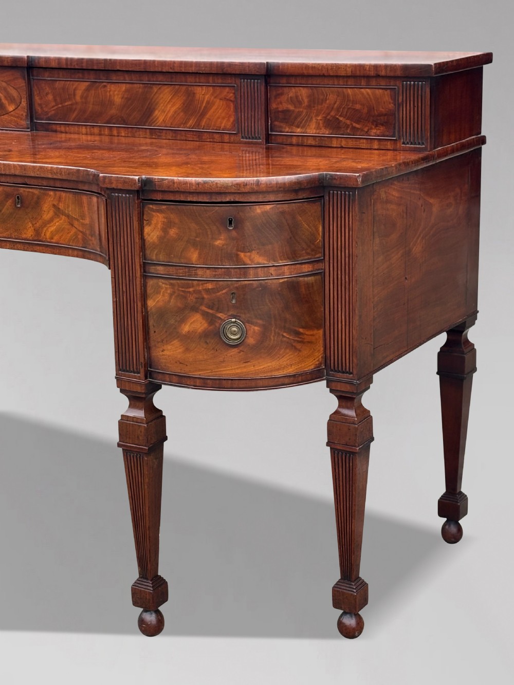 An 18th-century George III flame mahogany sideboard featuring a raised stage back, oval wood inlays, fluted side columns, and six turned reeded legs. View IV