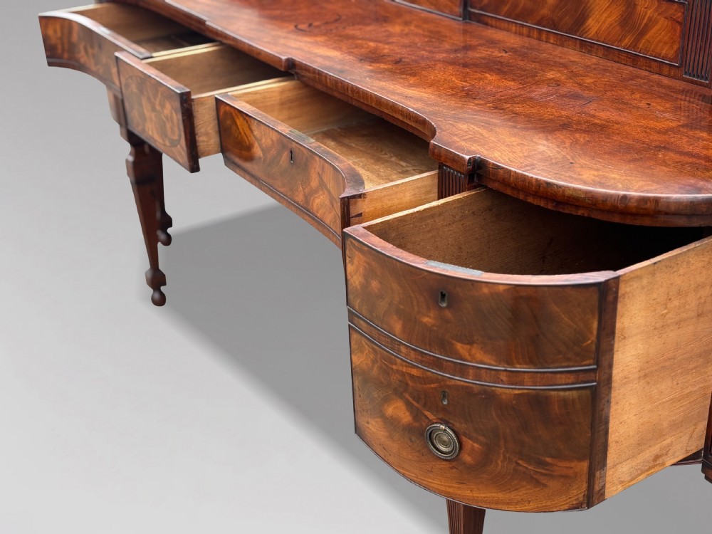 An 18th-century George III flame mahogany sideboard featuring a raised stage back, oval wood inlays, fluted side columns, and six turned reeded legs. View VI