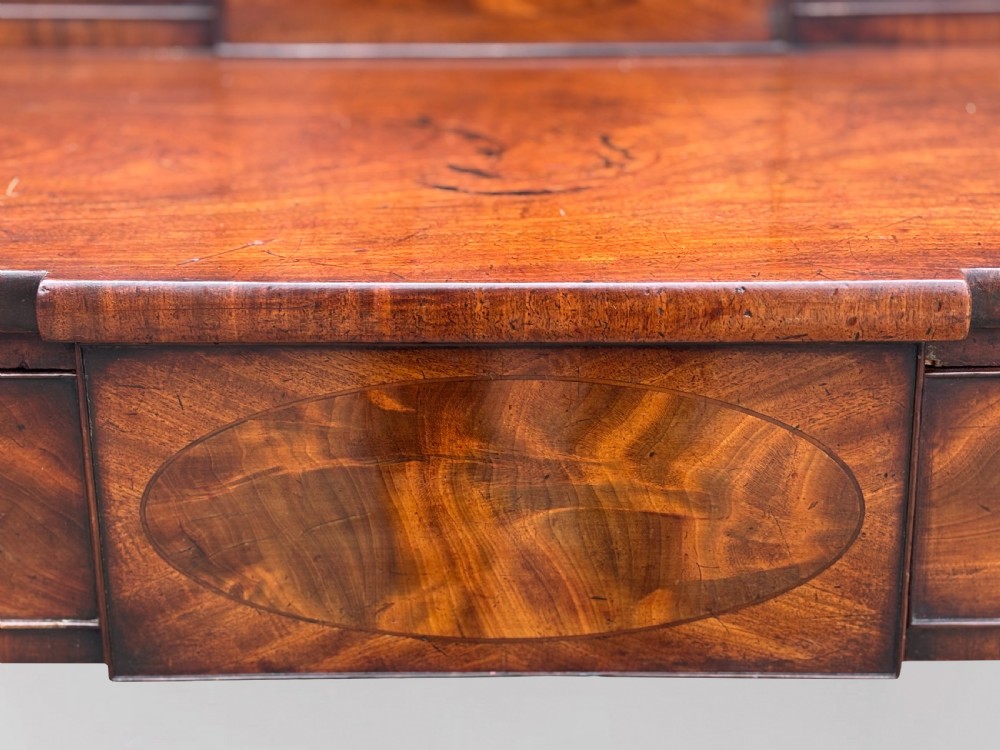 An 18th-century George III flame mahogany sideboard featuring a raised stage back, oval wood inlays, fluted side columns, and six turned reeded legs. View X