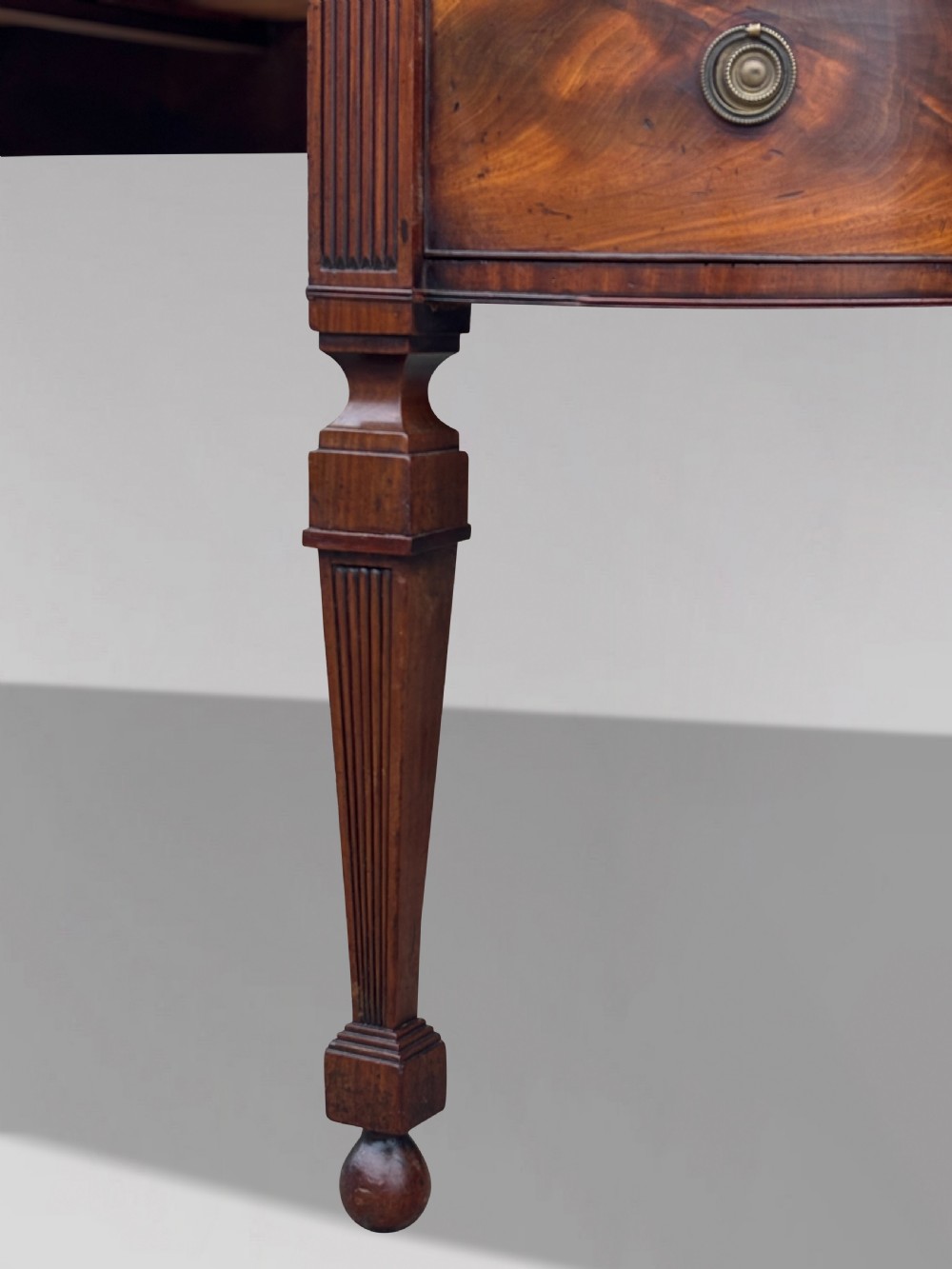 An 18th-century George III flame mahogany sideboard featuring a raised stage back, oval wood inlays, fluted side columns, and six turned reeded legs. View XI