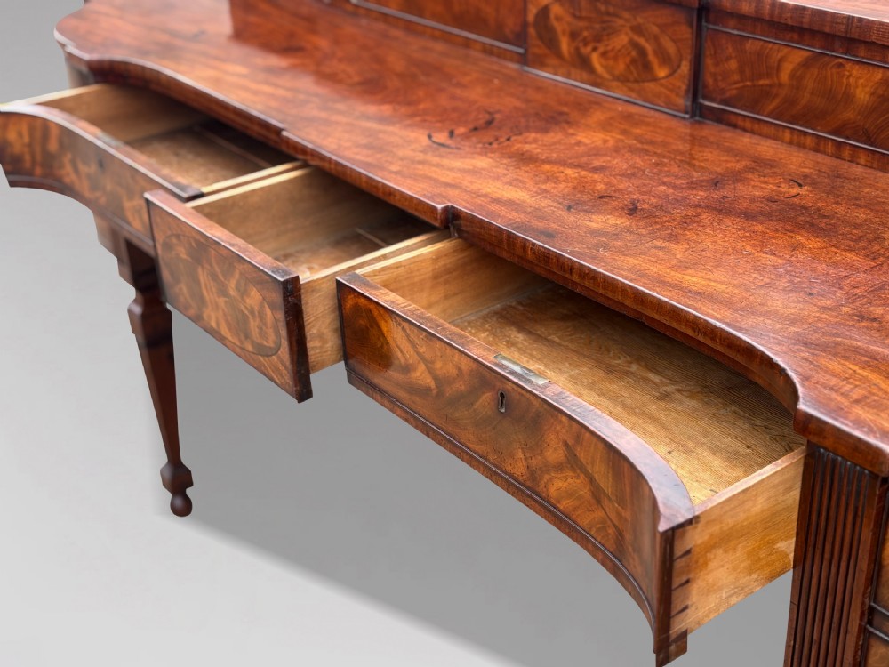 An 18th-century George III flame mahogany sideboard featuring a raised stage back, oval wood inlays, fluted side columns, and six turned reeded legs. View XII