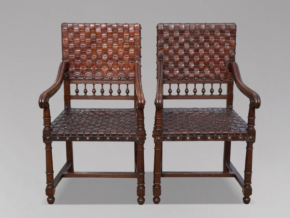 A pair of late 19th-century dark oak armchairs featuring woven brown leather backrests and seats with brass stud detailing and turned legs. View II