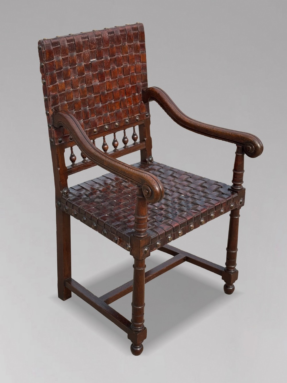 A pair of late 19th-century dark oak armchairs featuring woven brown leather backrests and seats with brass stud detailing and turned legs. View III