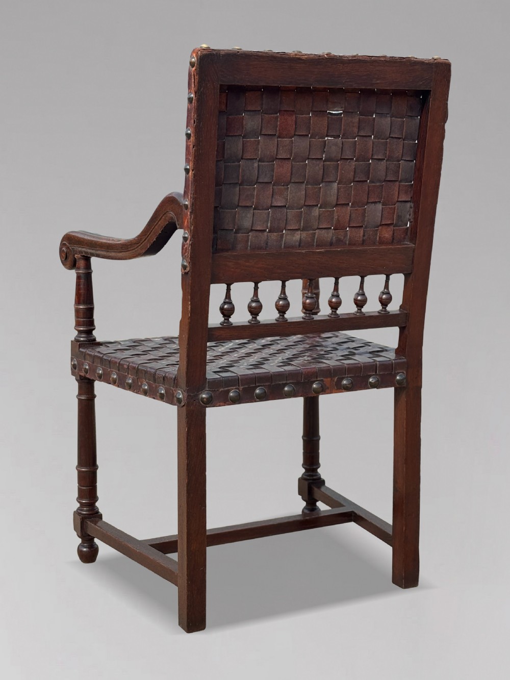 A pair of late 19th-century dark oak armchairs featuring woven brown leather backrests and seats with brass stud detailing and turned legs. View IV