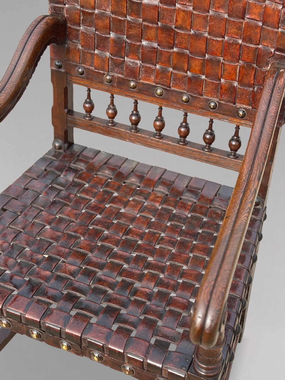 A pair of late 19th-century dark oak armchairs featuring woven brown leather backrests and seats with brass stud detailing and turned legs. View V
