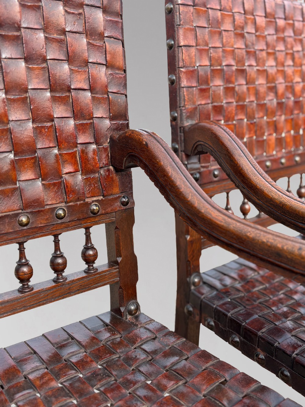 A pair of late 19th-century dark oak armchairs featuring woven brown leather backrests and seats with brass stud detailing and turned legs. View VI