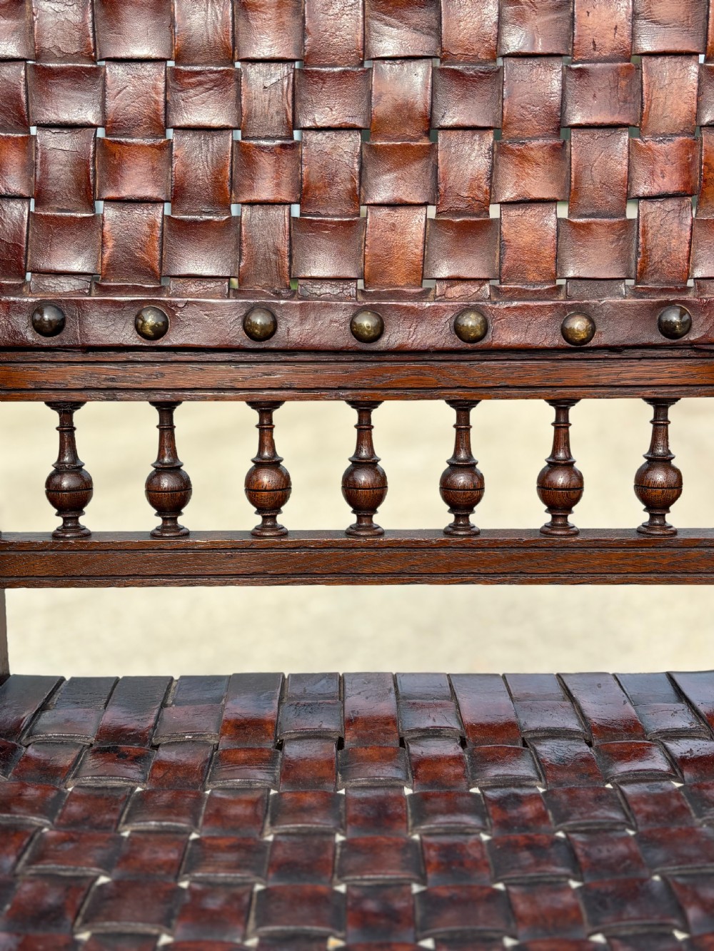 A pair of late 19th-century dark oak armchairs featuring woven brown leather backrests and seats with brass stud detailing and turned legs. View VII