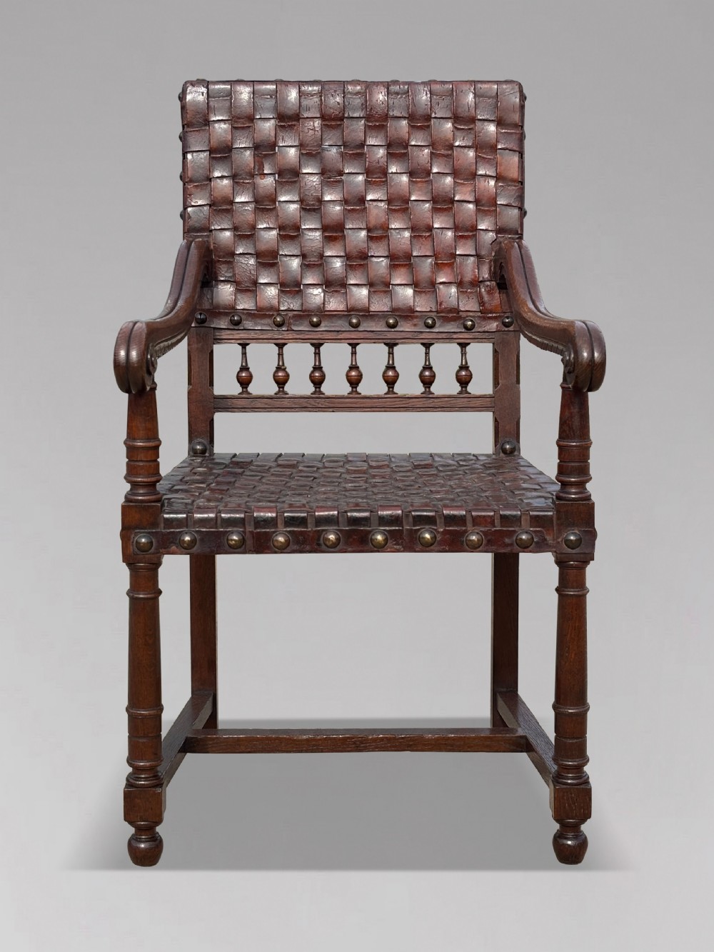A pair of late 19th-century dark oak armchairs featuring woven brown leather backrests and seats with brass stud detailing and turned legs. View VIII