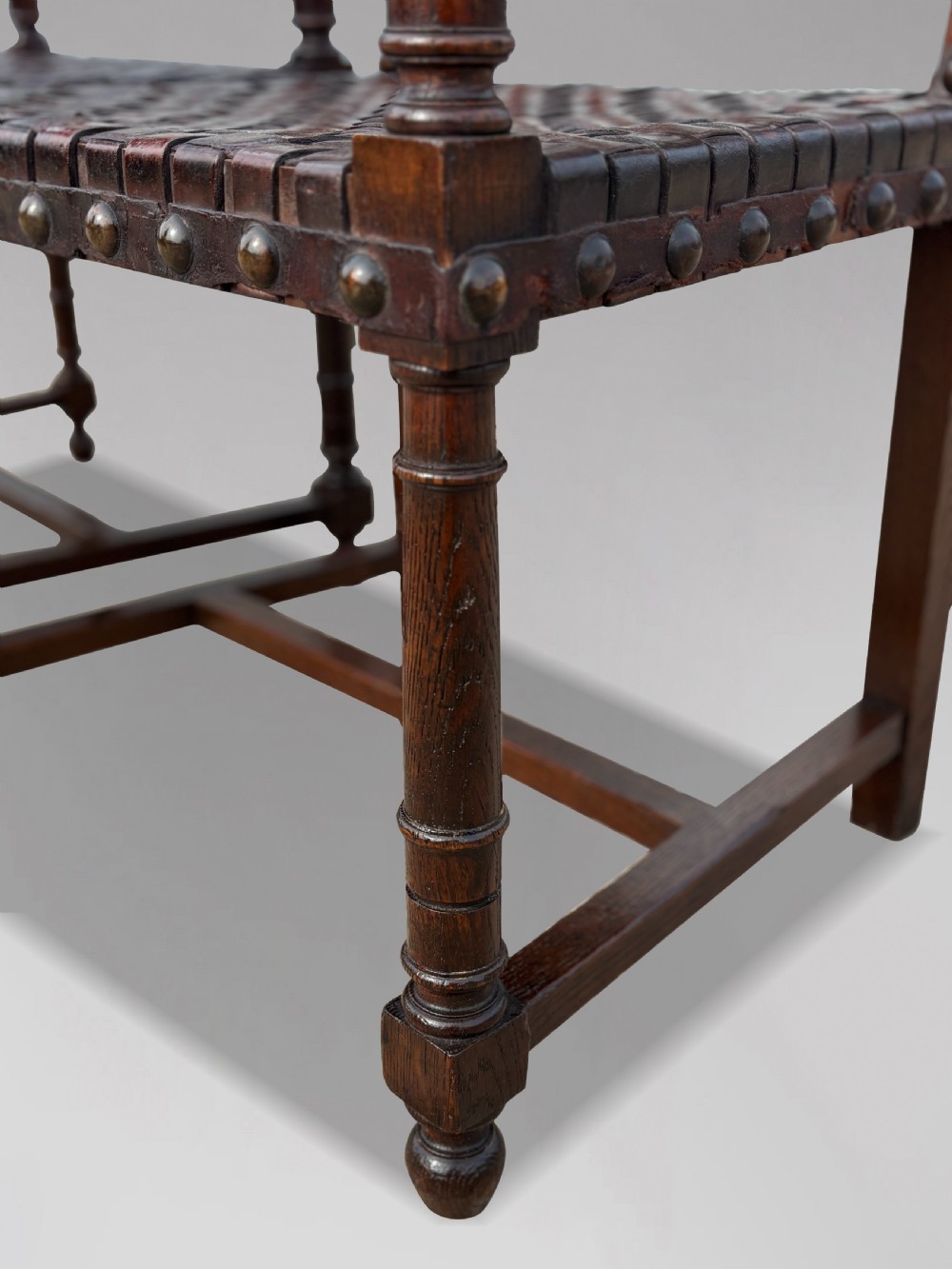 A pair of late 19th-century dark oak armchairs featuring woven brown leather backrests and seats with brass stud detailing and turned legs. View X