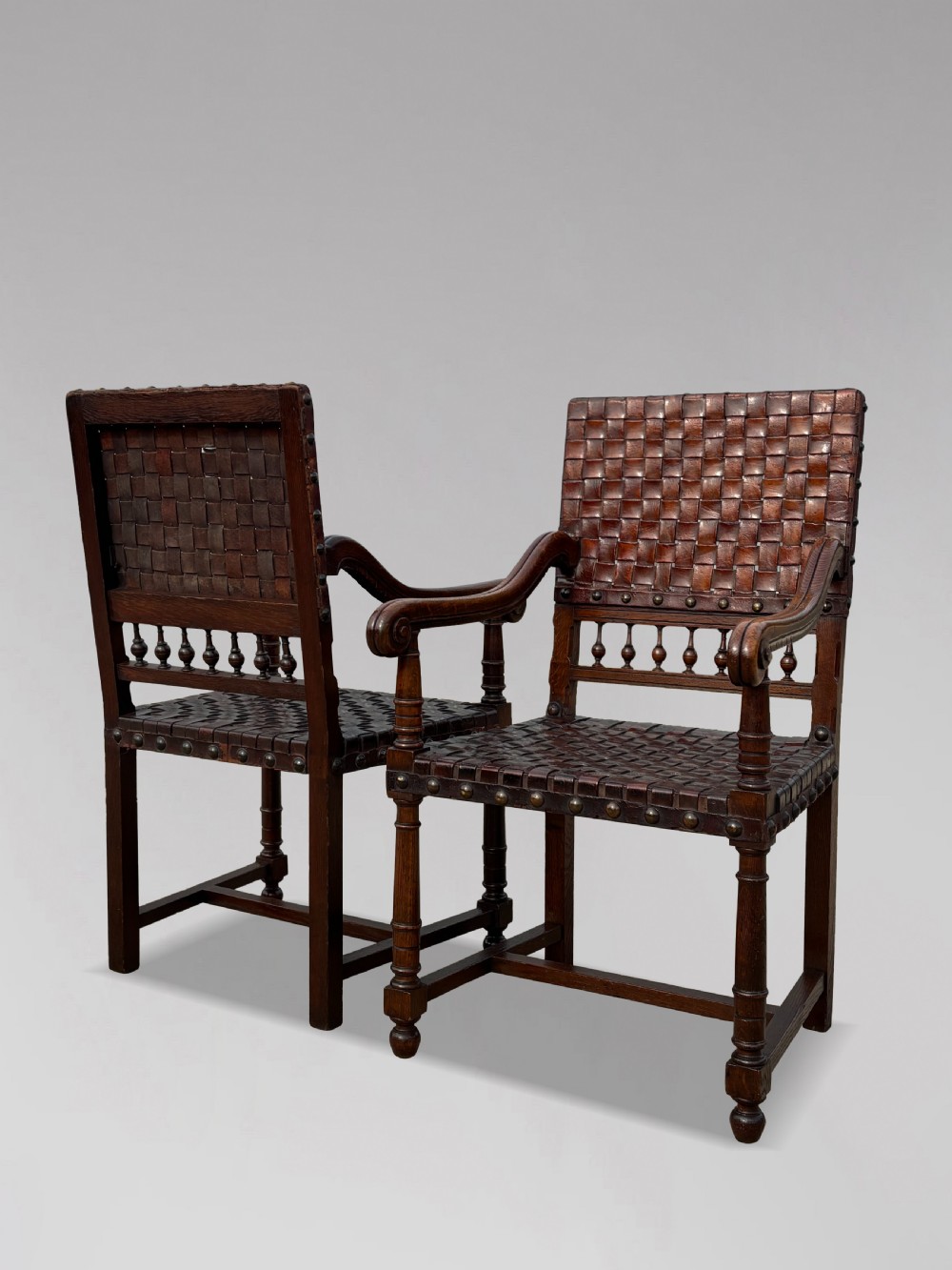 A pair of late 19th-century dark oak armchairs featuring woven brown leather backrests and seats with brass stud detailing and turned legs. View XI