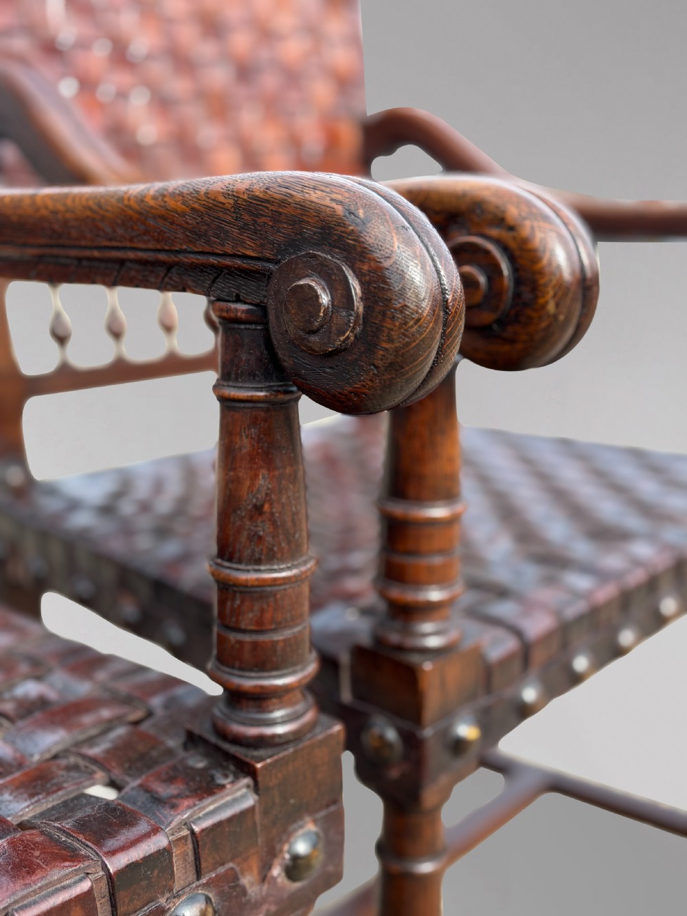 A pair of late 19th-century dark oak armchairs featuring woven brown leather backrests and seats with brass stud detailing and turned legs. View XII
