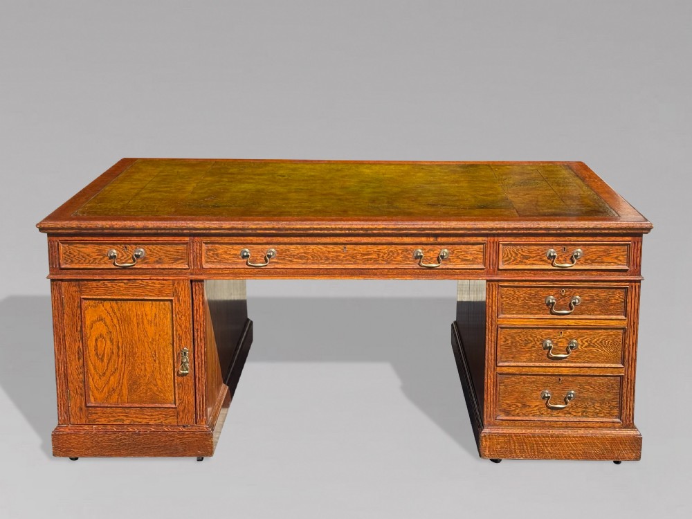A late 19th-century oak partners desk featuring a green leather inset writing surface, twin pedestals with drawers and cupboards, and brass hardware. View II