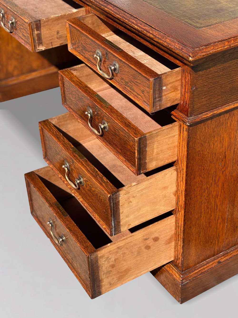 A late 19th-century oak partners desk featuring a green leather inset writing surface, twin pedestals with drawers and cupboards, and brass hardware. View V