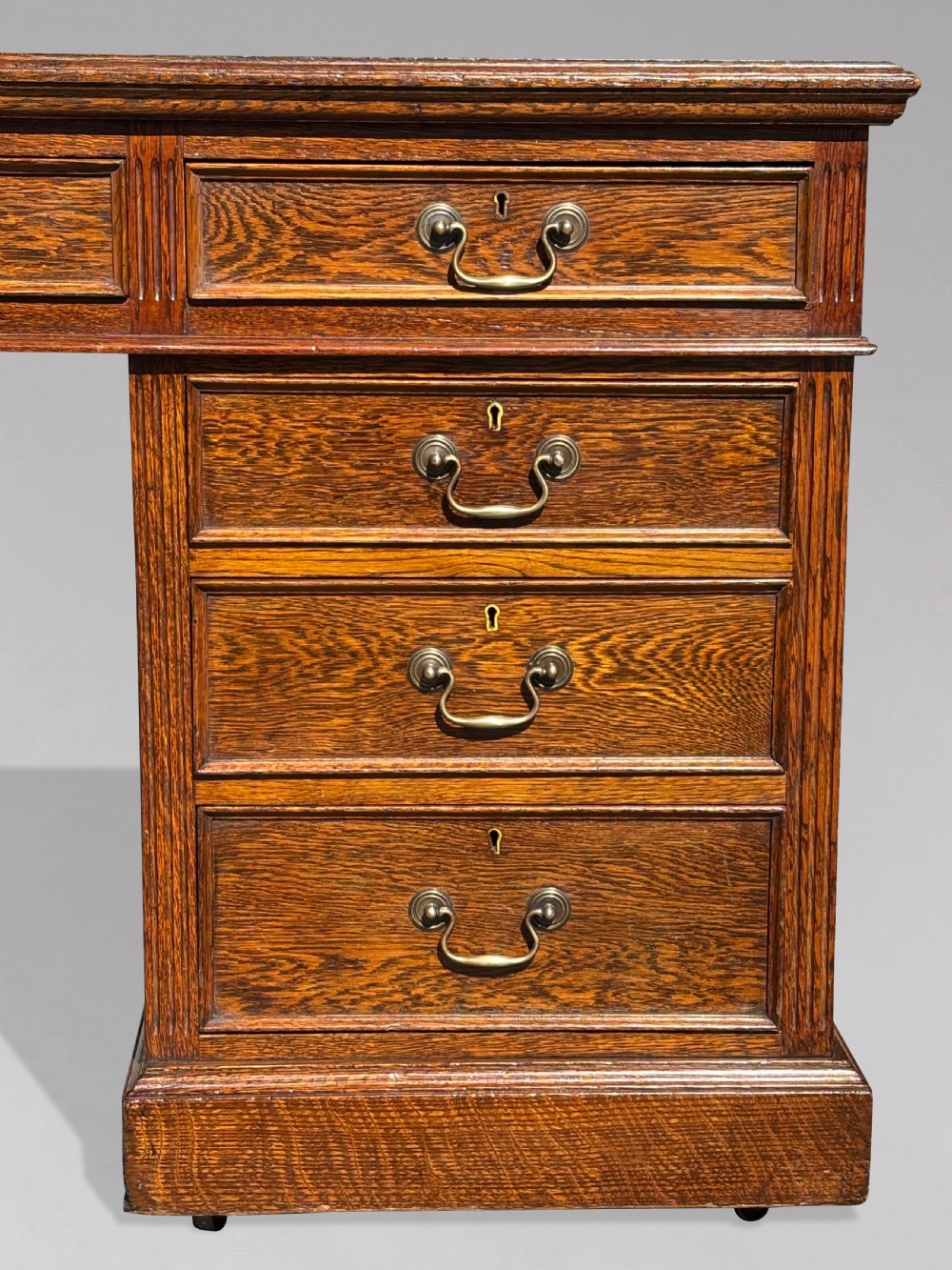 A late 19th-century oak partners desk featuring a green leather inset writing surface, twin pedestals with drawers and cupboards, and brass hardware. View VI