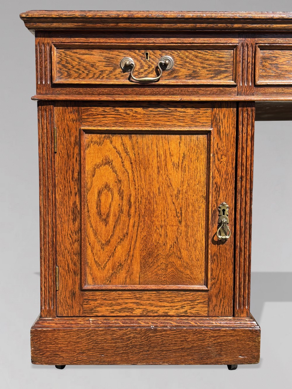 A late 19th-century oak partners desk featuring a green leather inset writing surface, twin pedestals with drawers and cupboards, and brass hardware. View VII