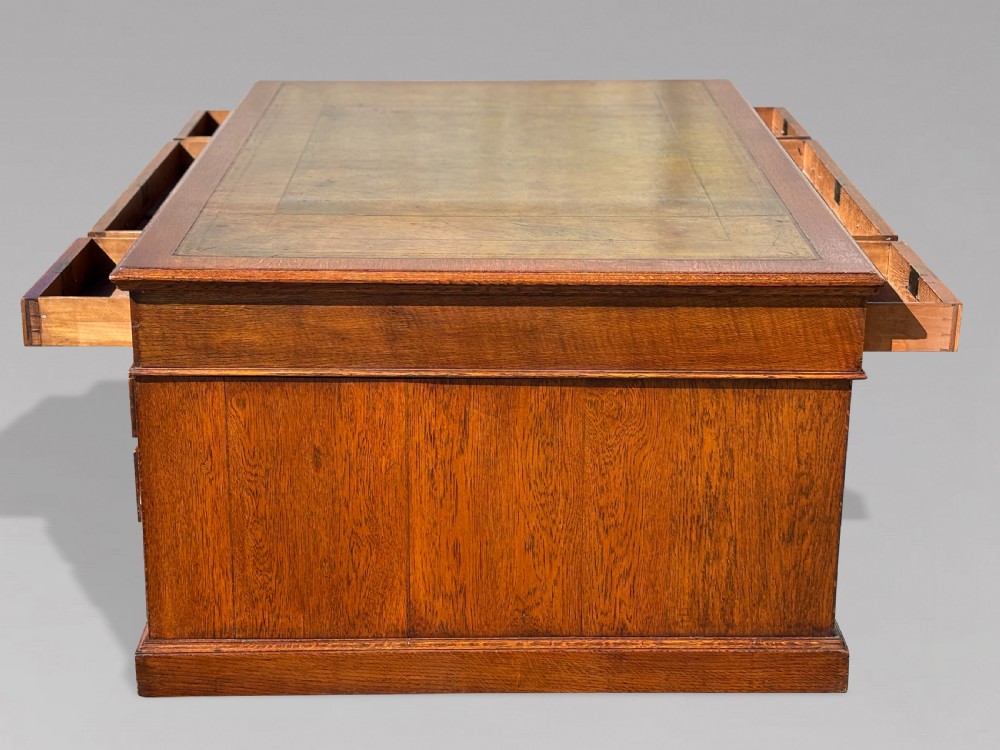 A late 19th-century oak partners desk featuring a green leather inset writing surface, twin pedestals with drawers and cupboards, and brass hardware. View VIII
