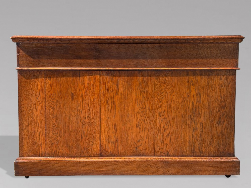 A late 19th-century oak partners desk featuring a green leather inset writing surface, twin pedestals with drawers and cupboards, and brass hardware. View IX