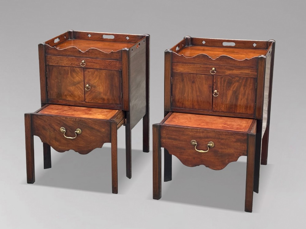 A pair of 18th-century George III mahogany bedside cabinets featuring tray tops with pierced handles, twin cupboard doors, and pull-out lower drawers with brass drop handles.