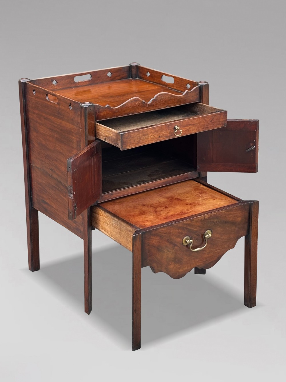 A pair of 18th-century George III mahogany bedside cabinets featuring tray tops with pierced handles, twin cupboard doors, and pull-out lower drawers with brass drop handles. View X