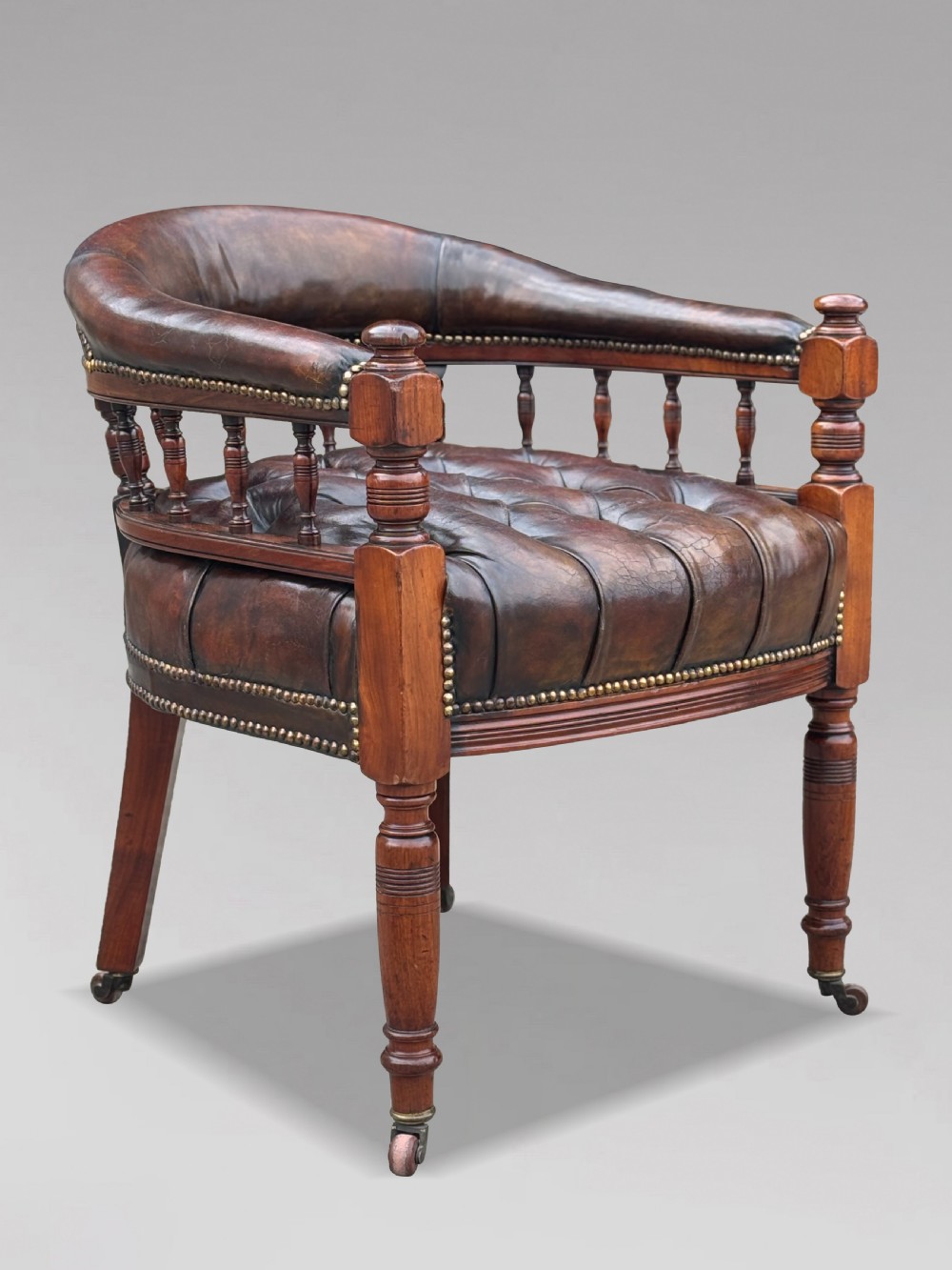 19th-century mahogany captains desk armchair upholstered in button-tufted brown leather with brass stud detail and turned spindles.