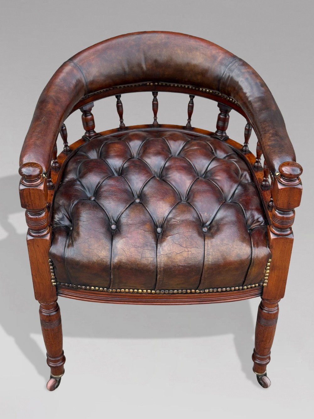 19th-century mahogany captains desk armchair upholstered in button-tufted brown leather with brass stud detail and turned spindles. View II