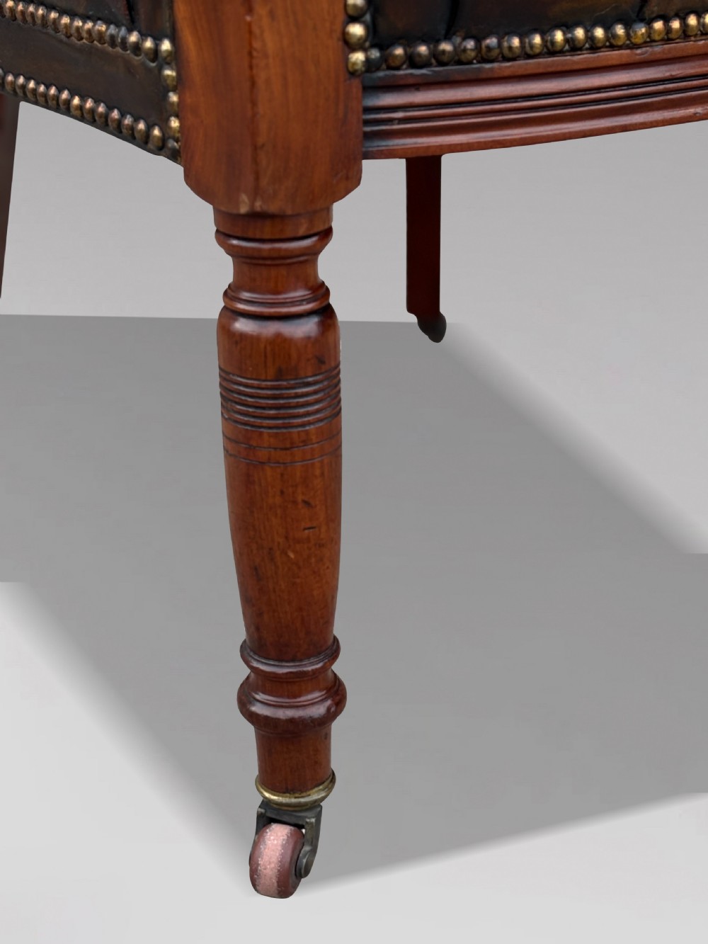 19th-century mahogany captains desk armchair upholstered in button-tufted brown leather with brass stud detail and turned spindles. View V