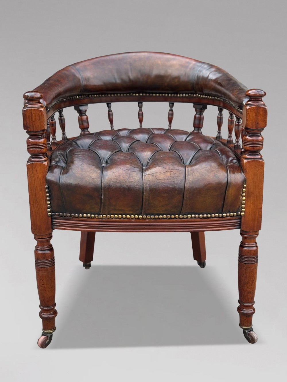 19th-century mahogany captains desk armchair upholstered in button-tufted brown leather with brass stud detail and turned spindles. View VI