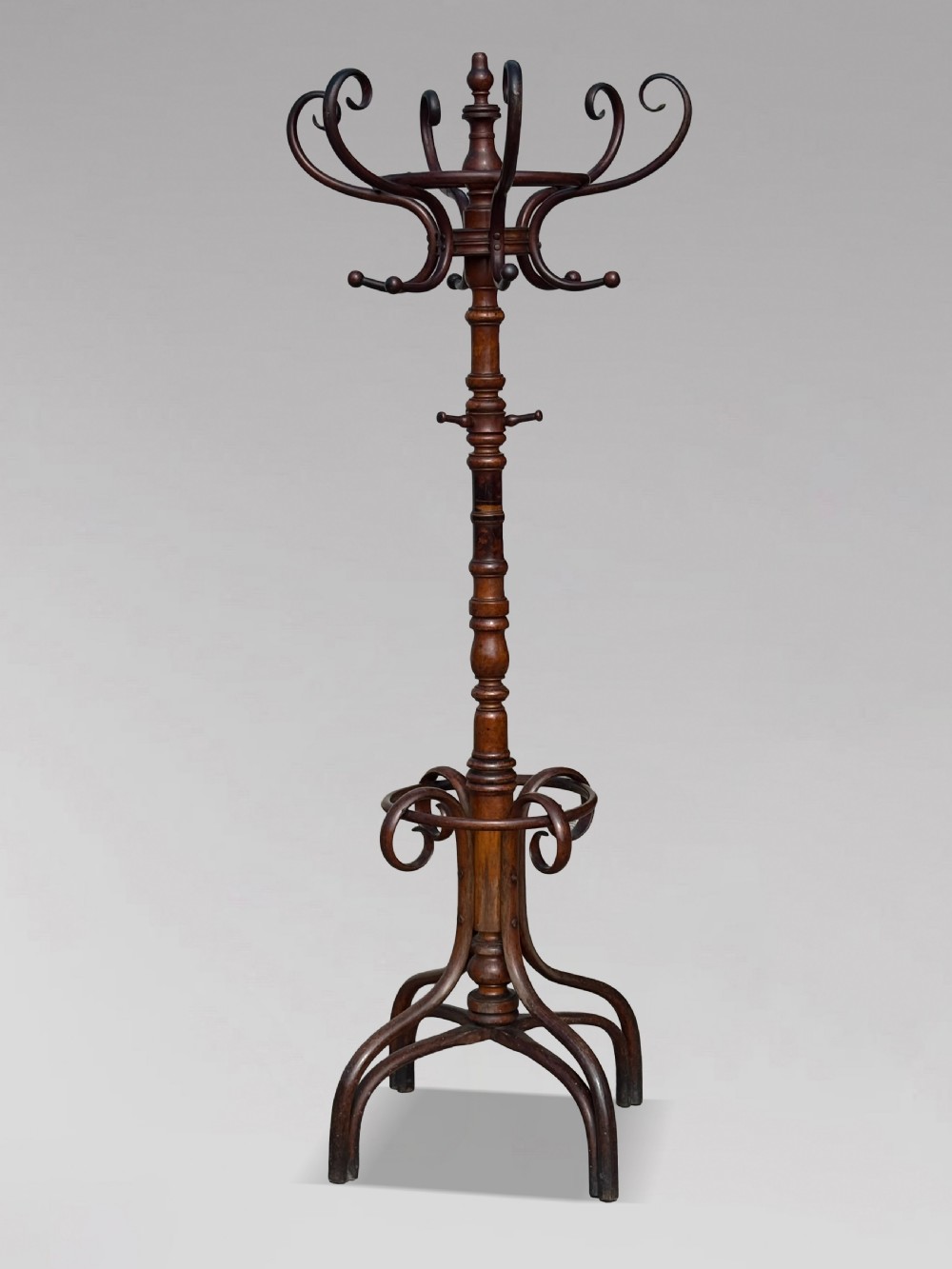 A dark brown bentwood hat and coat stand featuring upper scrolled hooks, a turned central column, a lower umbrella ring, and curved feet.