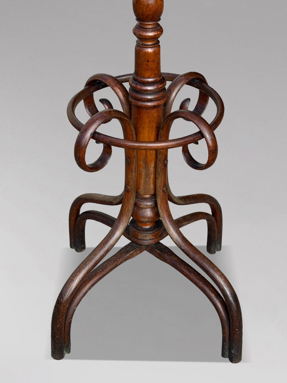 A dark brown bentwood hat and coat stand featuring upper scrolled hooks, a turned central column, a lower umbrella ring, and curved feet. View II