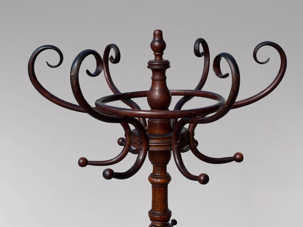 A dark brown bentwood hat and coat stand featuring upper scrolled hooks, a turned central column, a lower umbrella ring, and curved feet. View III