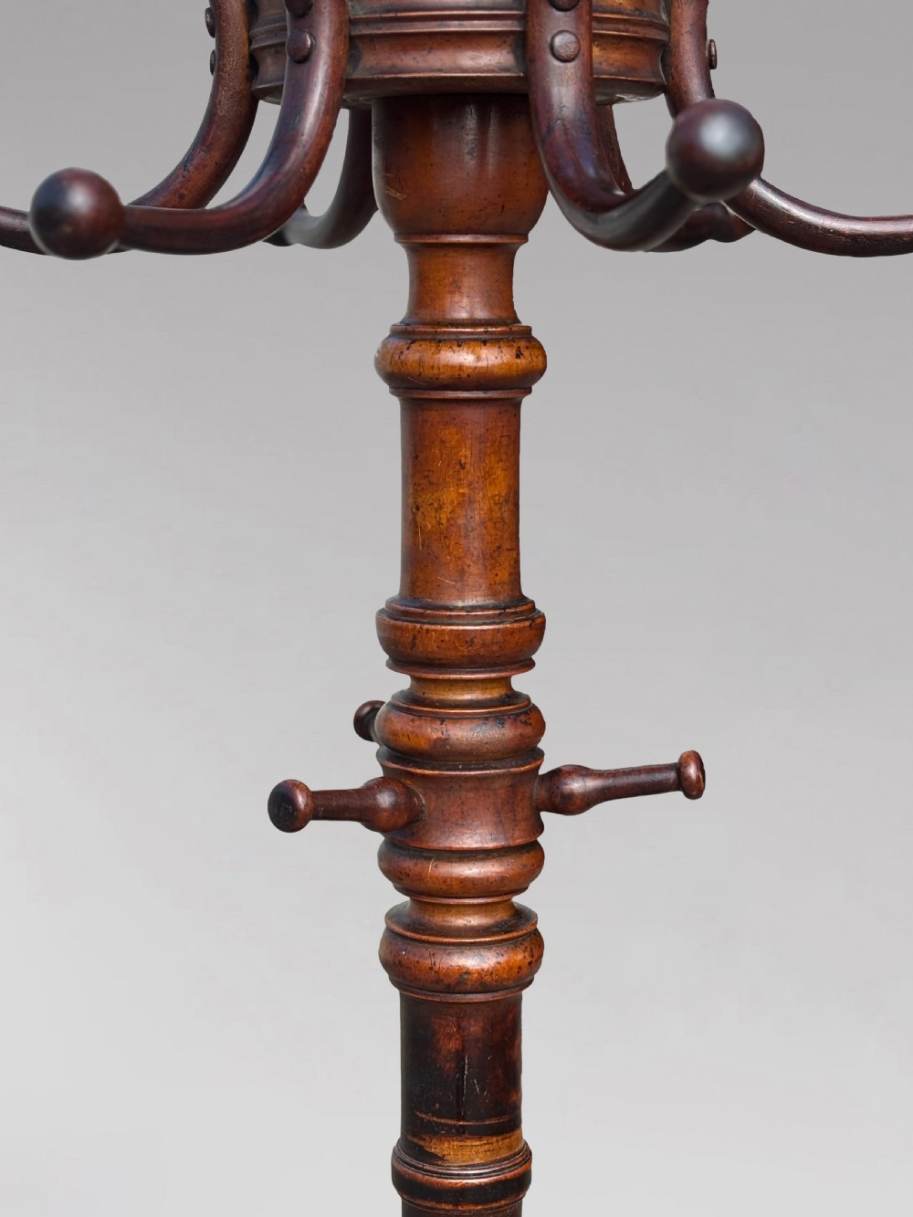 A dark brown bentwood hat and coat stand featuring upper scrolled hooks, a turned central column, a lower umbrella ring, and curved feet. View VI