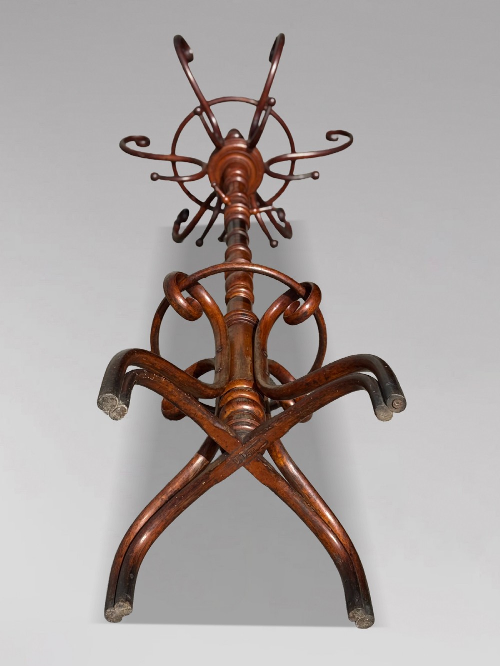 A dark brown bentwood hat and coat stand featuring upper scrolled hooks, a turned central column, a lower umbrella ring, and curved feet. View VII