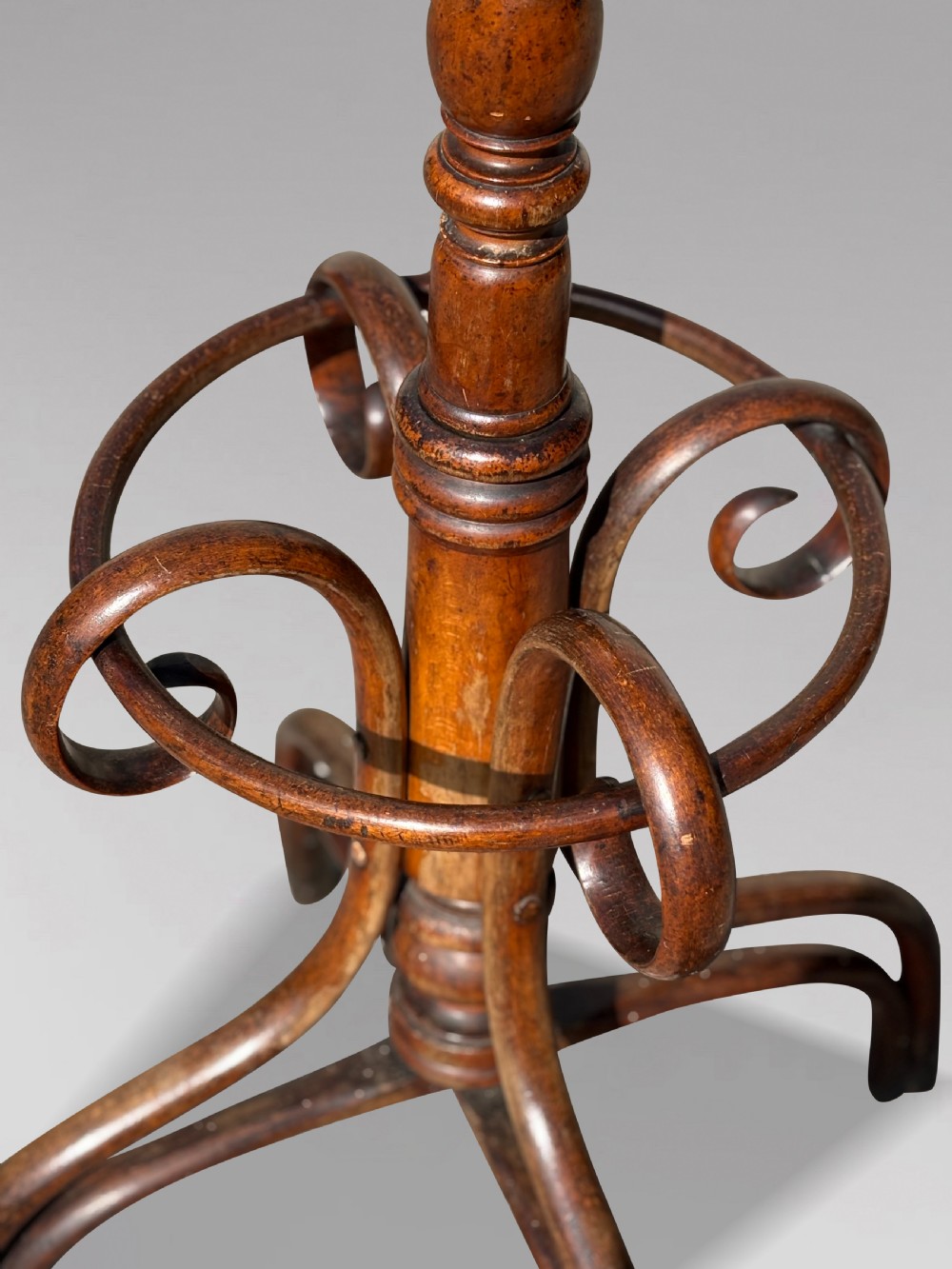 A dark brown bentwood hat and coat stand featuring upper scrolled hooks, a turned central column, a lower umbrella ring, and curved feet. View VIII