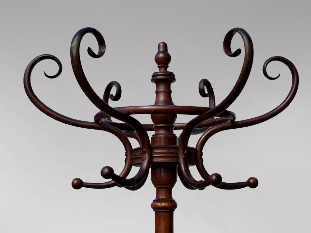 A dark brown bentwood hat and coat stand featuring upper scrolled hooks, a turned central column, a lower umbrella ring, and curved feet. View X