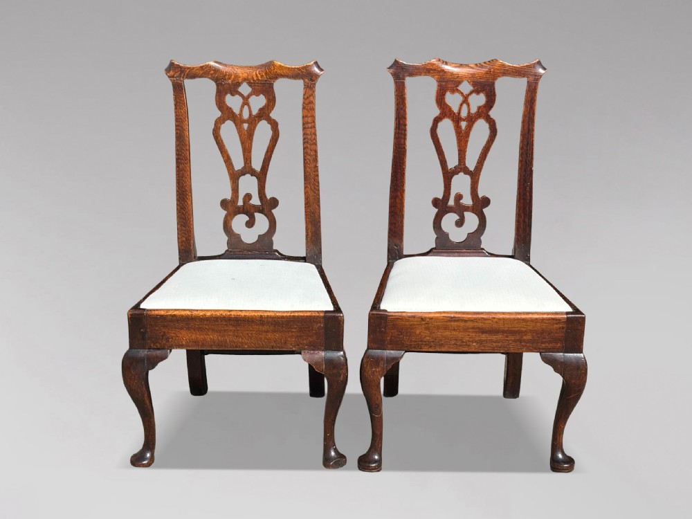 A pair of 18th-century George III oak Chippendale side chairs featuring carved pierced splats, upholstered drop-in seats, and cabriole front legs.