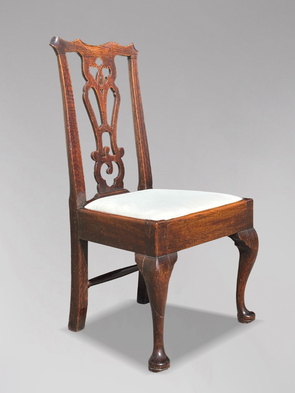 A pair of 18th-century George III oak Chippendale side chairs featuring carved pierced splats, upholstered drop-in seats, and cabriole front legs. View V