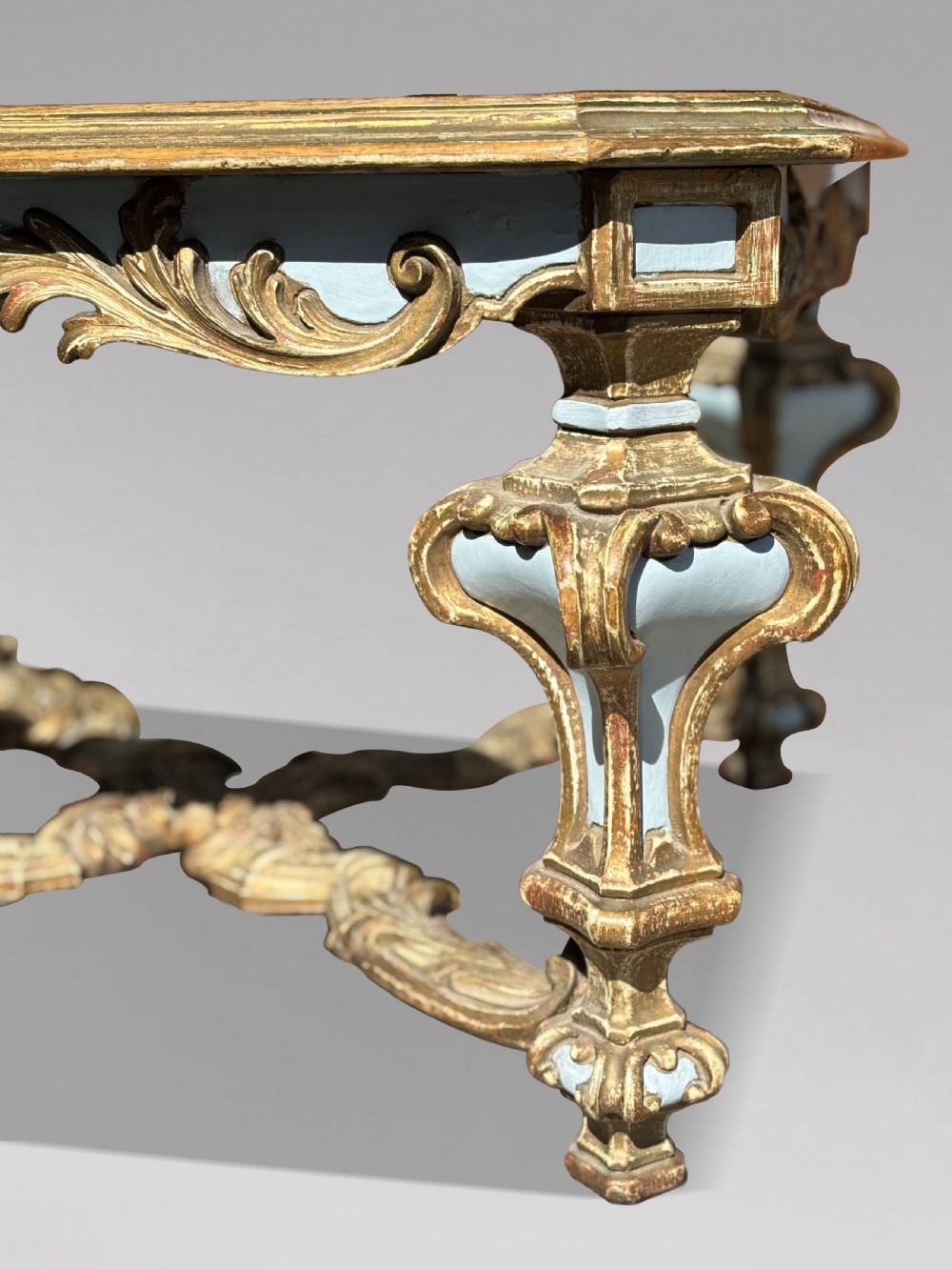 A square Italian Baroque style coffee table featuring a glass top, pale blue paint finish, carved gilt scrollwork frieze, ornate scrolled legs, and an X-shaped stretcher. View VIII