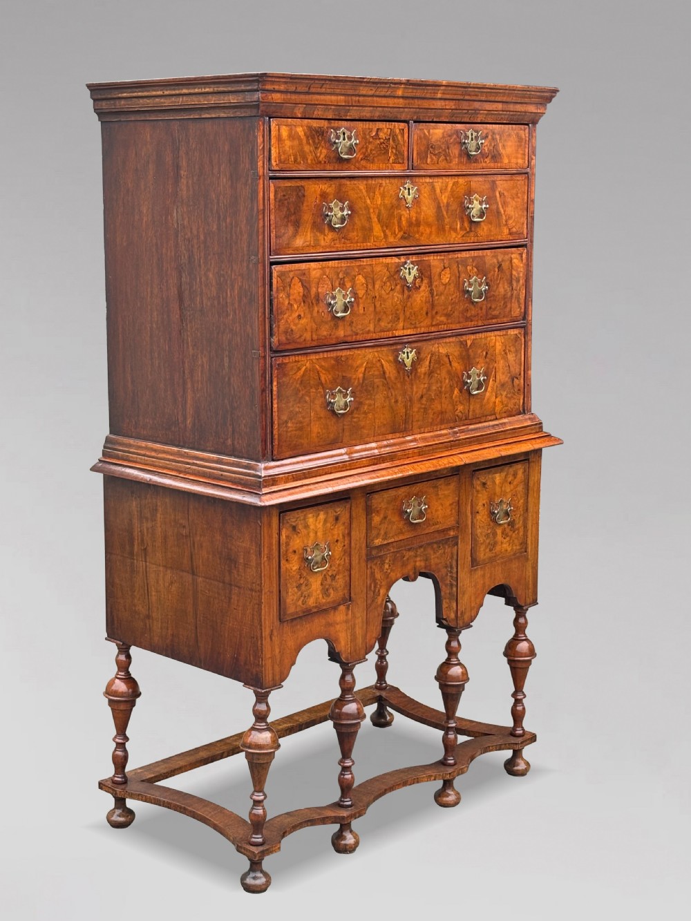 An 18th-century Queen Anne walnut chest on stand featuring figured veneers, brass drop handles, a shaped lower apron, and turned legs joined by stretchers. View II