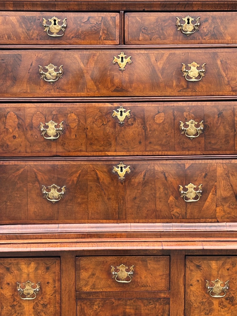 An 18th-century Queen Anne walnut chest on stand featuring figured veneers, brass drop handles, a shaped lower apron, and turned legs joined by stretchers. View III