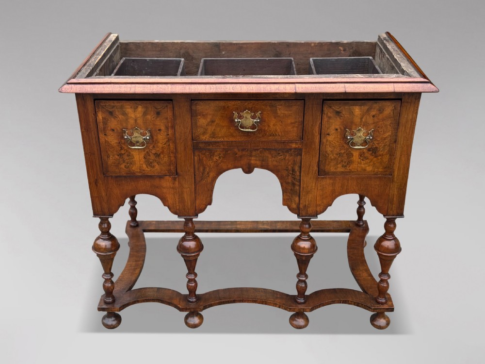 An 18th-century Queen Anne walnut chest on stand featuring figured veneers, brass drop handles, a shaped lower apron, and turned legs joined by stretchers. View VI
