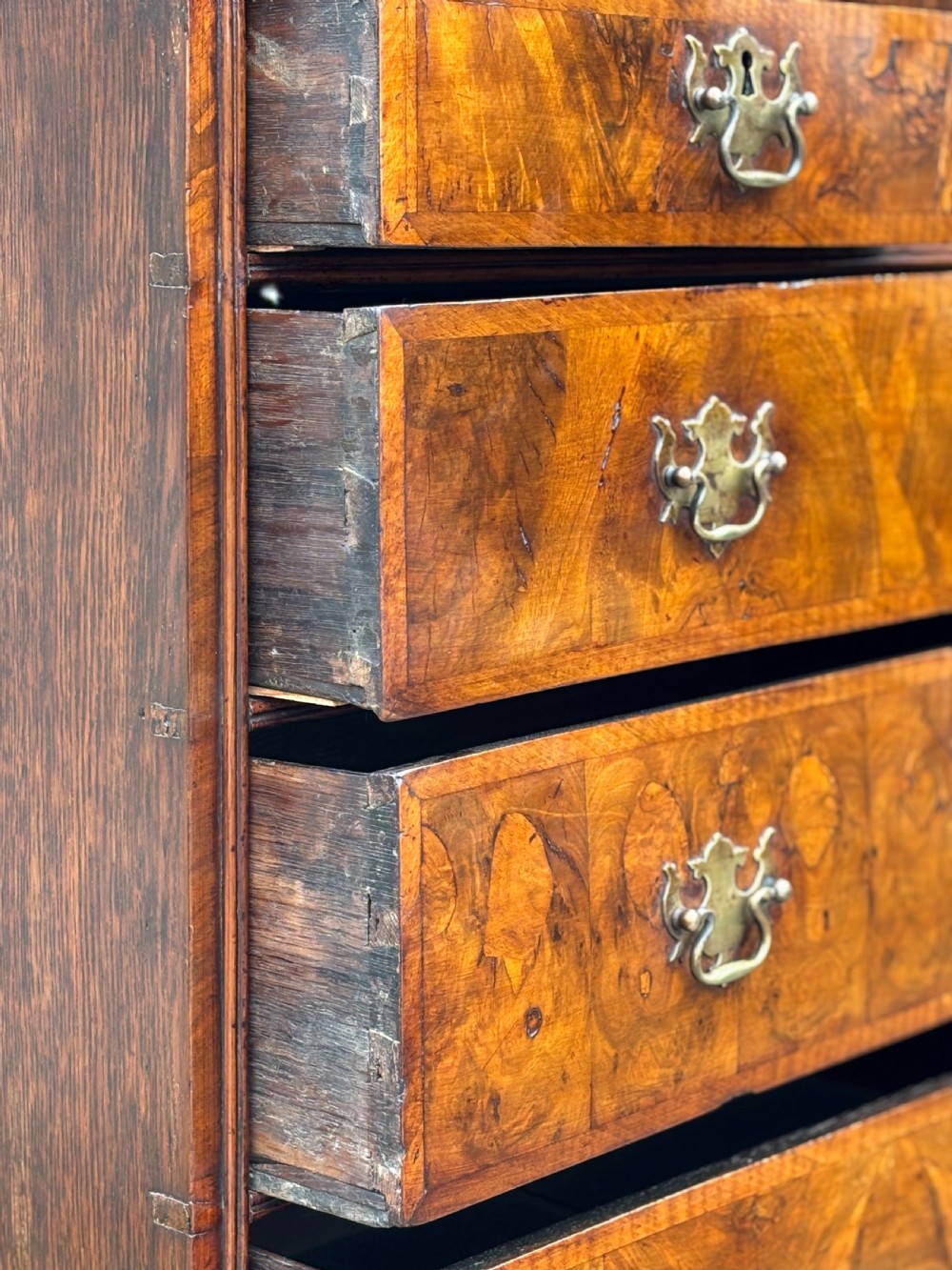 An 18th-century Queen Anne walnut chest on stand featuring figured veneers, brass drop handles, a shaped lower apron, and turned legs joined by stretchers. View VII