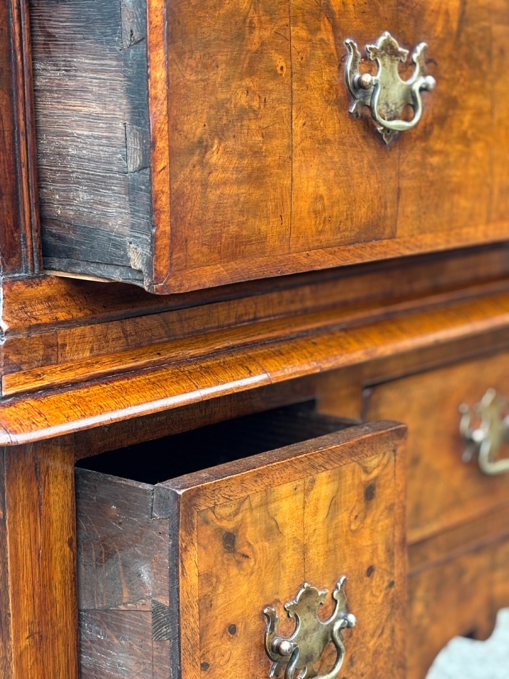 An 18th-century Queen Anne walnut chest on stand featuring figured veneers, brass drop handles, a shaped lower apron, and turned legs joined by stretchers. View VIII