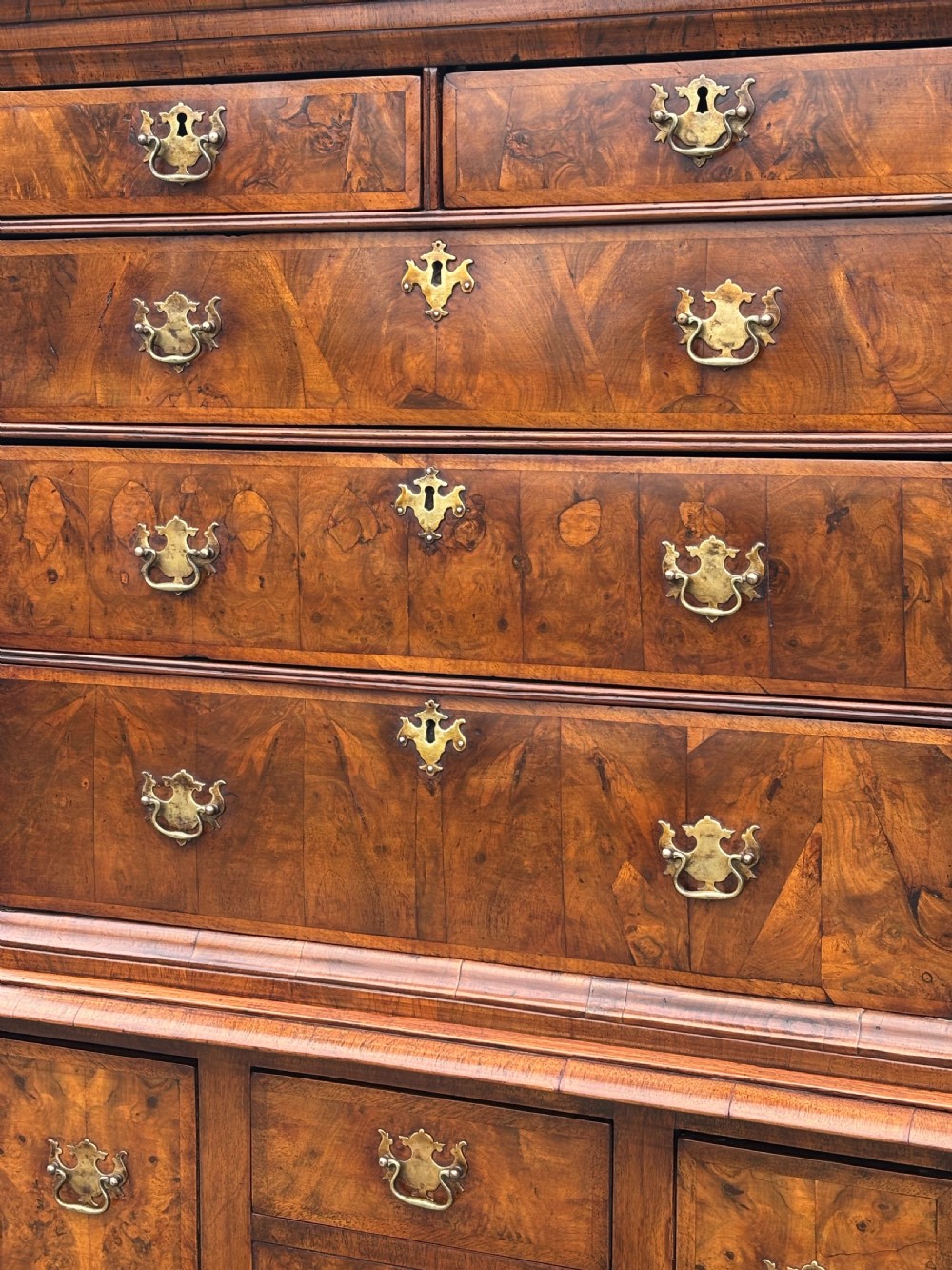 An 18th-century Queen Anne walnut chest on stand featuring figured veneers, brass drop handles, a shaped lower apron, and turned legs joined by stretchers. View IX