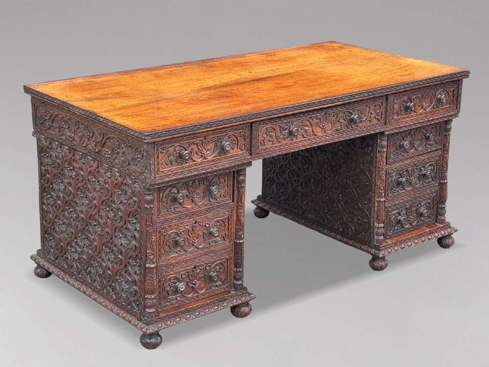 Nineteenth-century Anglo-Indian carved padauk partners desk featuring intricate foliate relief carvings across the pedestal drawers and side panels on turned bun feet.
