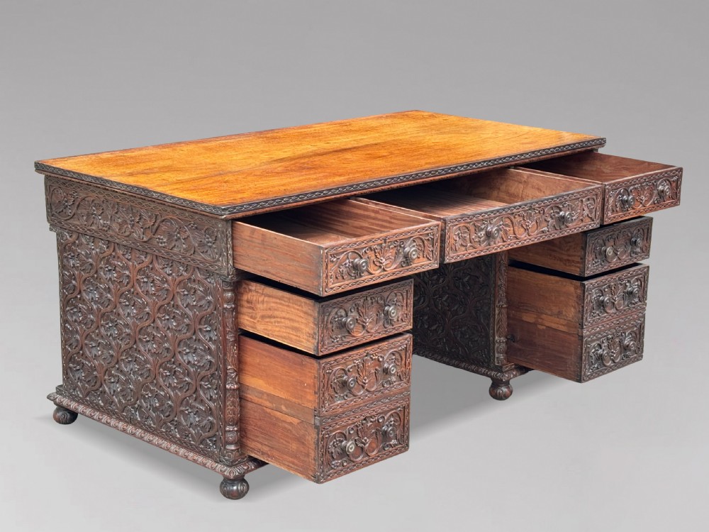 Nineteenth-century Anglo-Indian carved padauk partners desk featuring intricate foliate relief carvings across the pedestal drawers and side panels on turned bun feet. View V