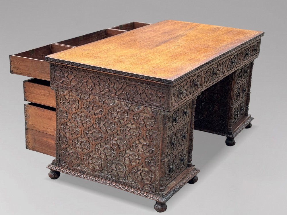 Nineteenth-century Anglo-Indian carved padauk partners desk featuring intricate foliate relief carvings across the pedestal drawers and side panels on turned bun feet. View IX