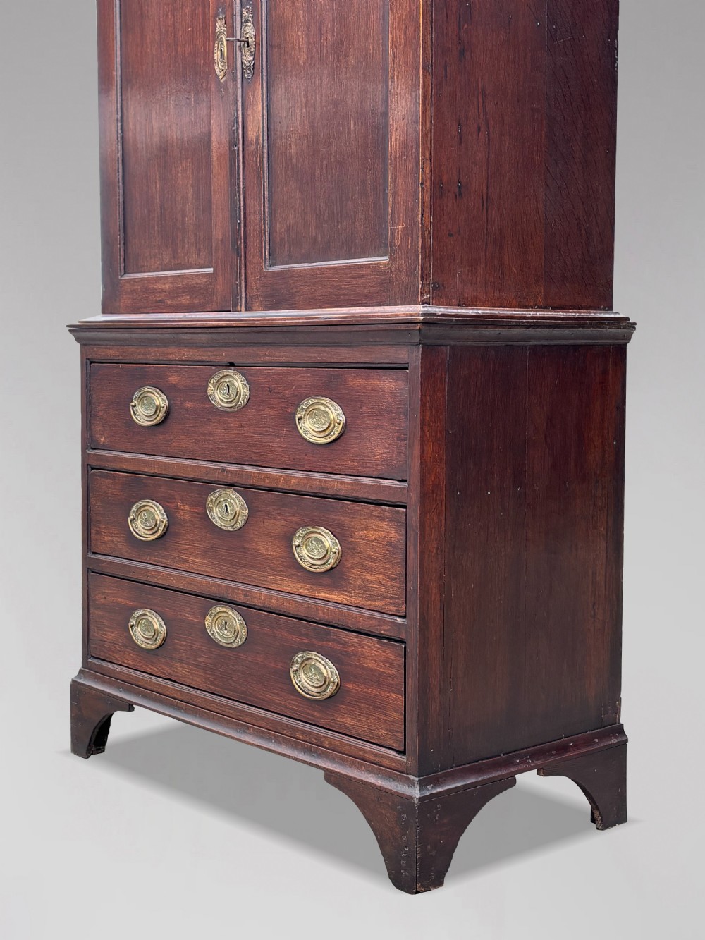 An 18th-century George III dark oak housekeepers cupboard featuring a fretwork gallery with a central turned finial, two upper panel doors, and three lower drawers with brass oval handles. View IV